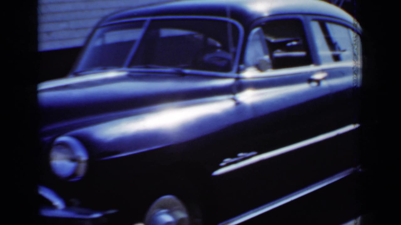 Black mid-century sedan seen close from the side on a sunny residential street.
