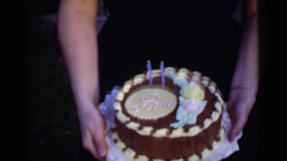 Close home-movie view of a decorated birthday cake with candles, held outdoors in 1950 New York footage.