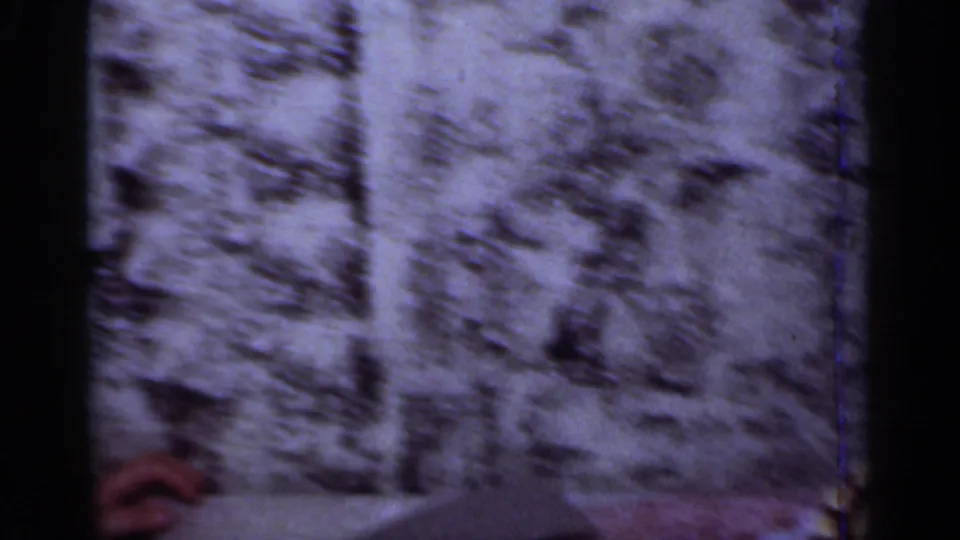 A soft, grainy 8mm frame of a textured interior wall in the New York birthday-party clip.