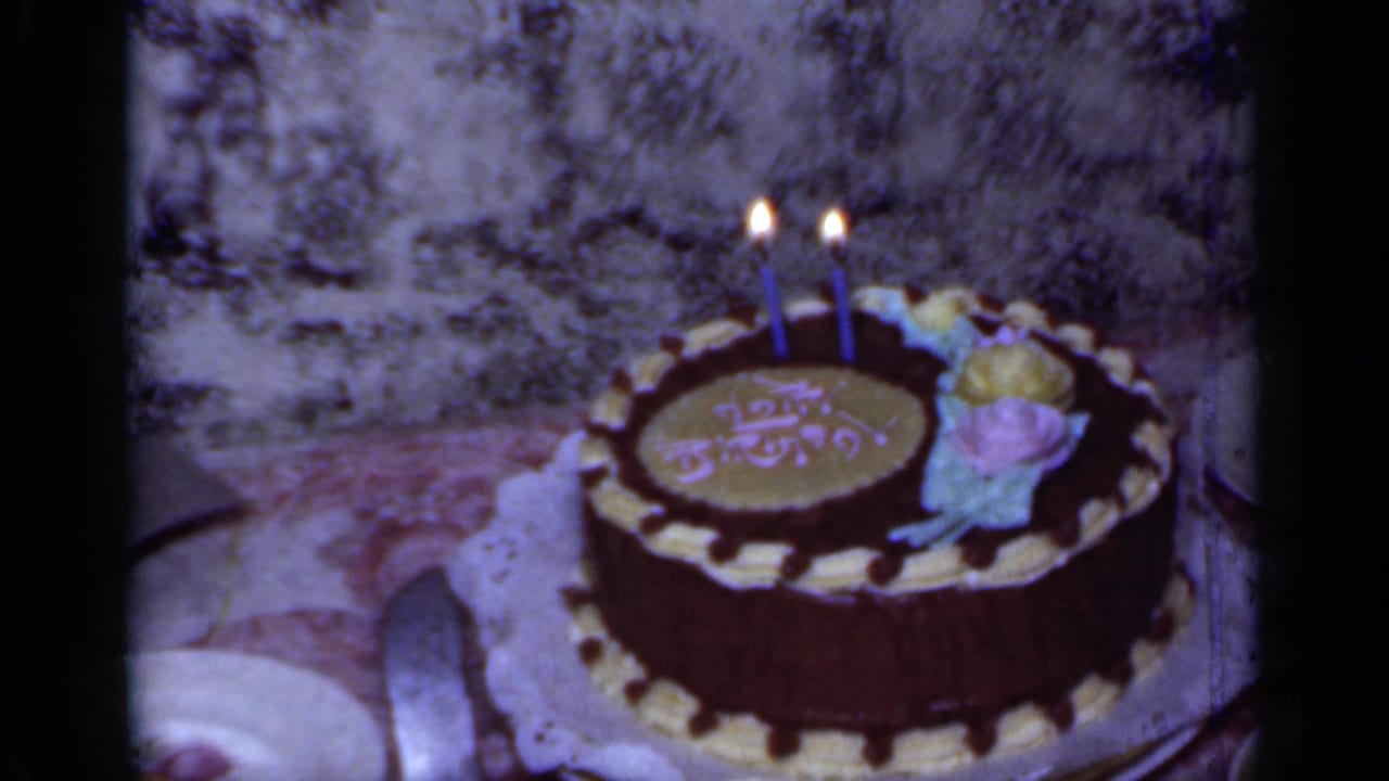 Chocolate birthday cake with lit candles on a table.