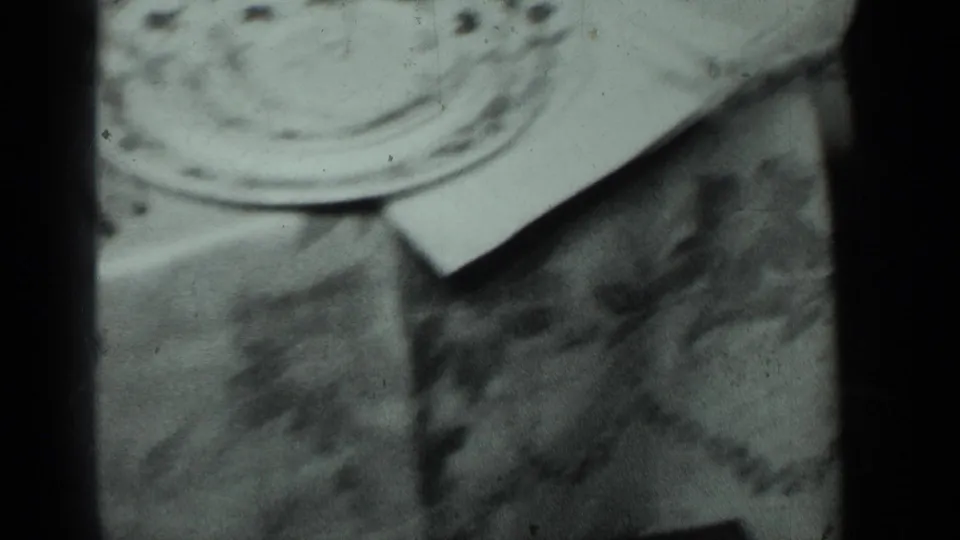 1950 New York 8mm close-up of patterned china, a folded white napkin, and a floral tablecloth during a slow tabletop pan.