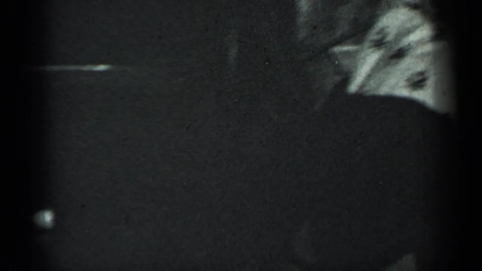 1950 New York 8mm frame showing a dark tabletop or furniture edge with a partial patterned plate and floral tablecloth at the side.