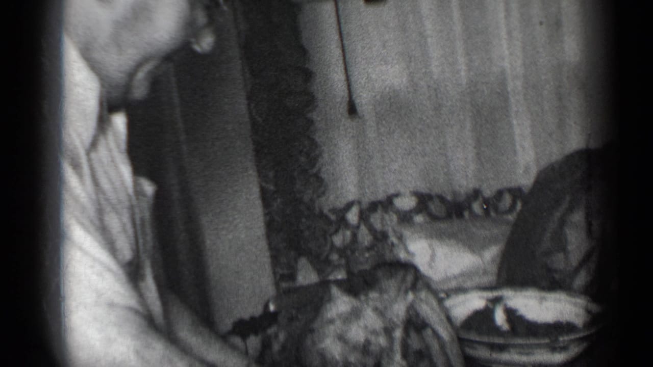 Man in glasses leans over a table while cutting meat with a large knife indoors.