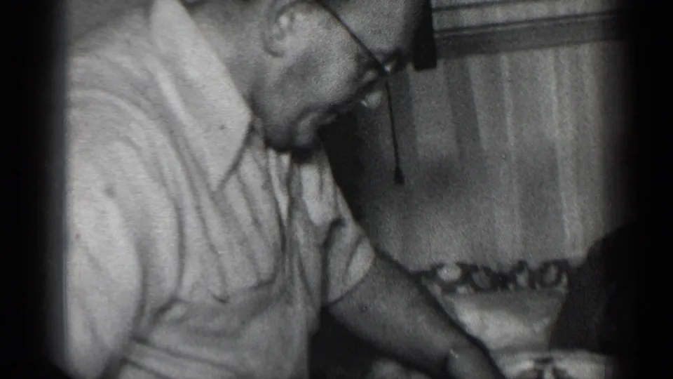 The man remains bent over the tabletop, with glasses, short sleeves, meat, and dishware visible in the 8mm frame.