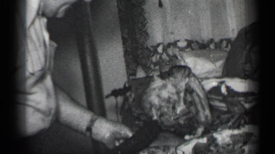 A close 8mm view shows the man's wristwatch, hand, knife, and meat on the table in a private indoor setting.