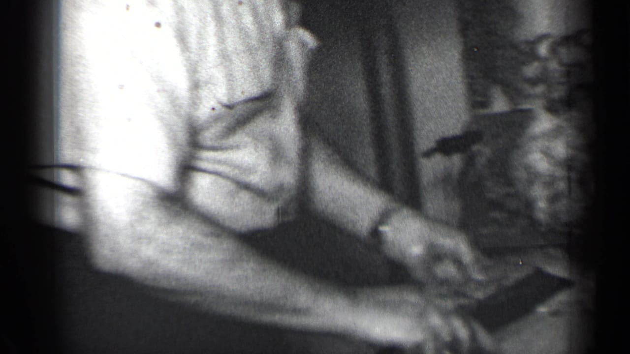 Man's hands carve a turkey on a dining table in grainy black-and-white footage.