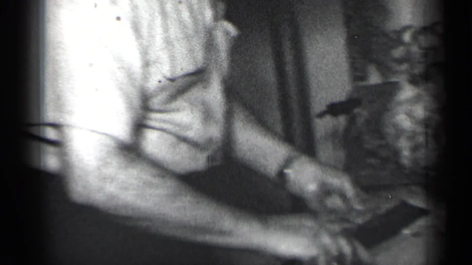 In 1950 New York home-movie footage, a man in a short-sleeved shirt carves a turkey at an indoor dining table.