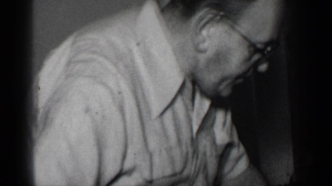 Man in glasses leans over while carving food at a dark indoor table.