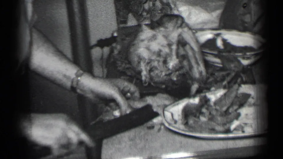 The turkey sits partly carved on the dining table while a hand reaches near a serving plate in the home-movie frame.