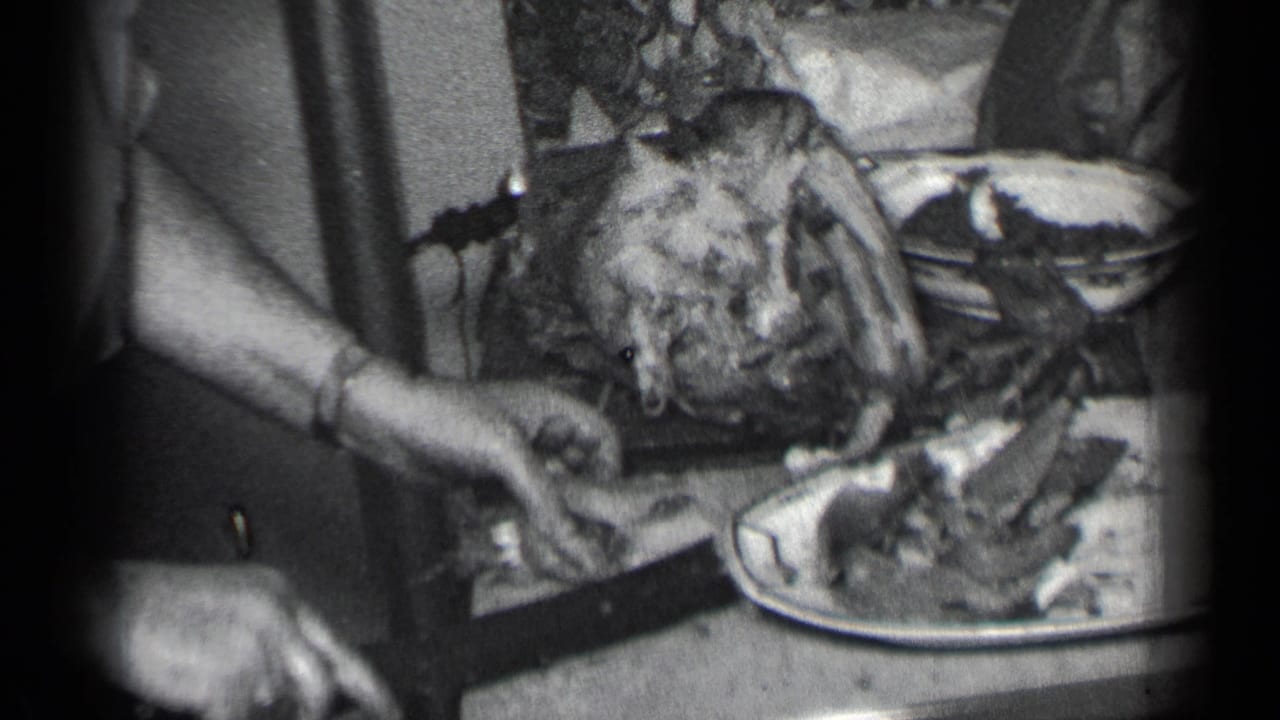 Hands carve a roasted turkey on a table while a serving plate sits nearby.