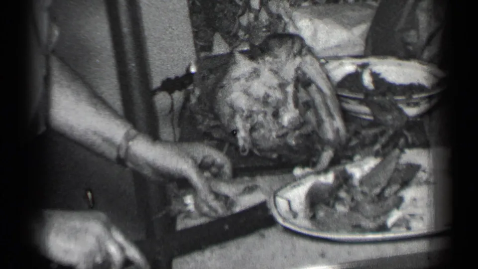 In this 1950 New York 8mm home-movie frame, hands carve a large roasted turkey at a crowded household table.