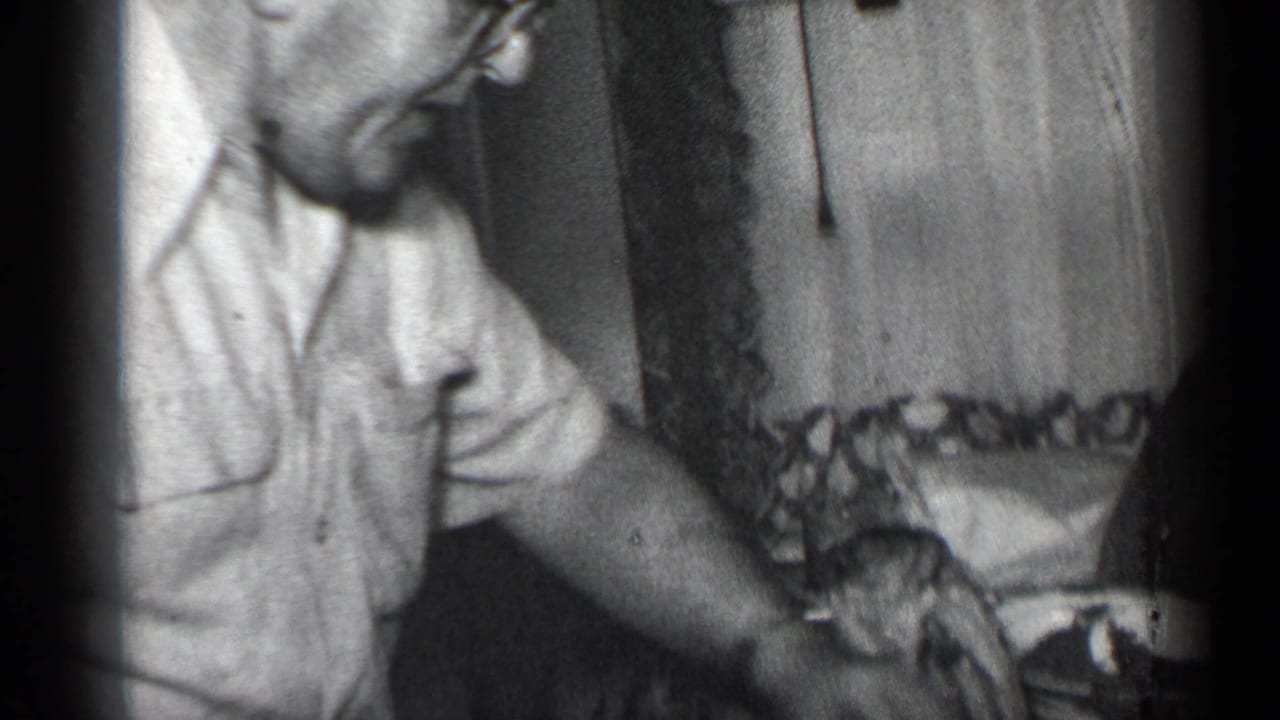 A man in glasses and a short-sleeved shirt sits beside the holiday table in the 1950 New York home-movie footage.