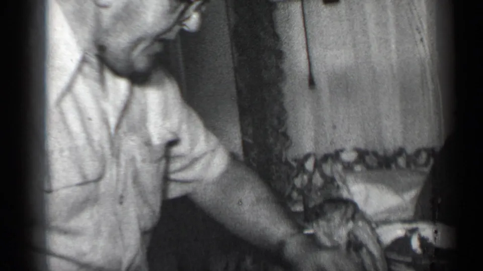 A man in glasses and a short-sleeved shirt sits beside the holiday table in the 1950 New York home-movie footage.