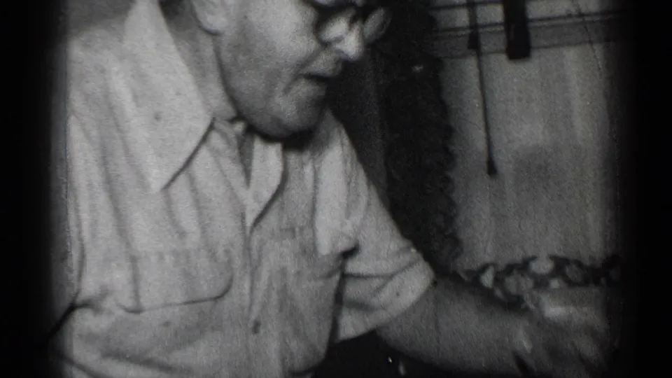 The man appears in close profile inside the private New York interior, looking down as food is handled near the table.