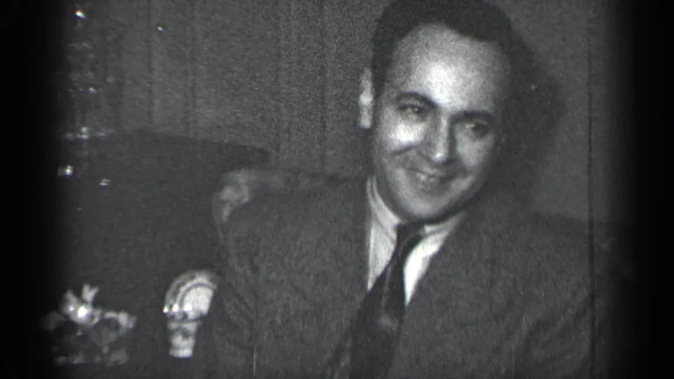 The 1950 New York 8mm frame shows a smiling man in formal dress near small tabletop decorations indoors.
