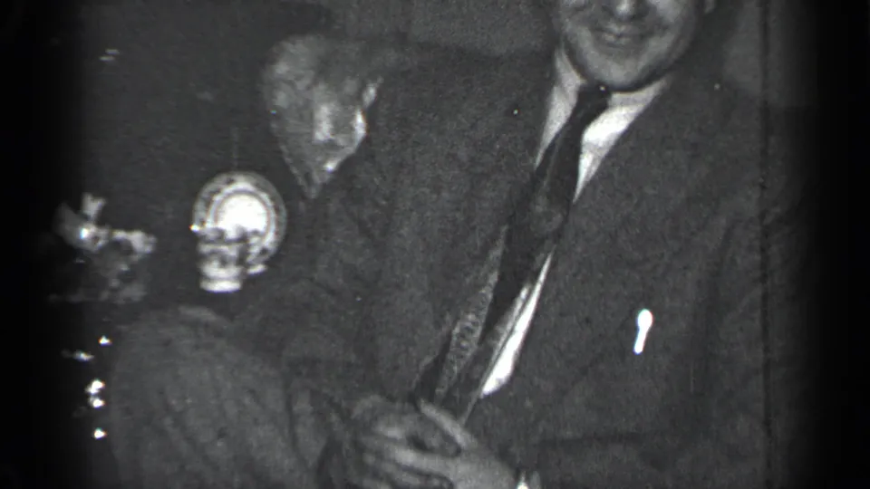 1950 New York 8mm frame of suited men seated indoors, with one man laughing during a close informal exchange.
