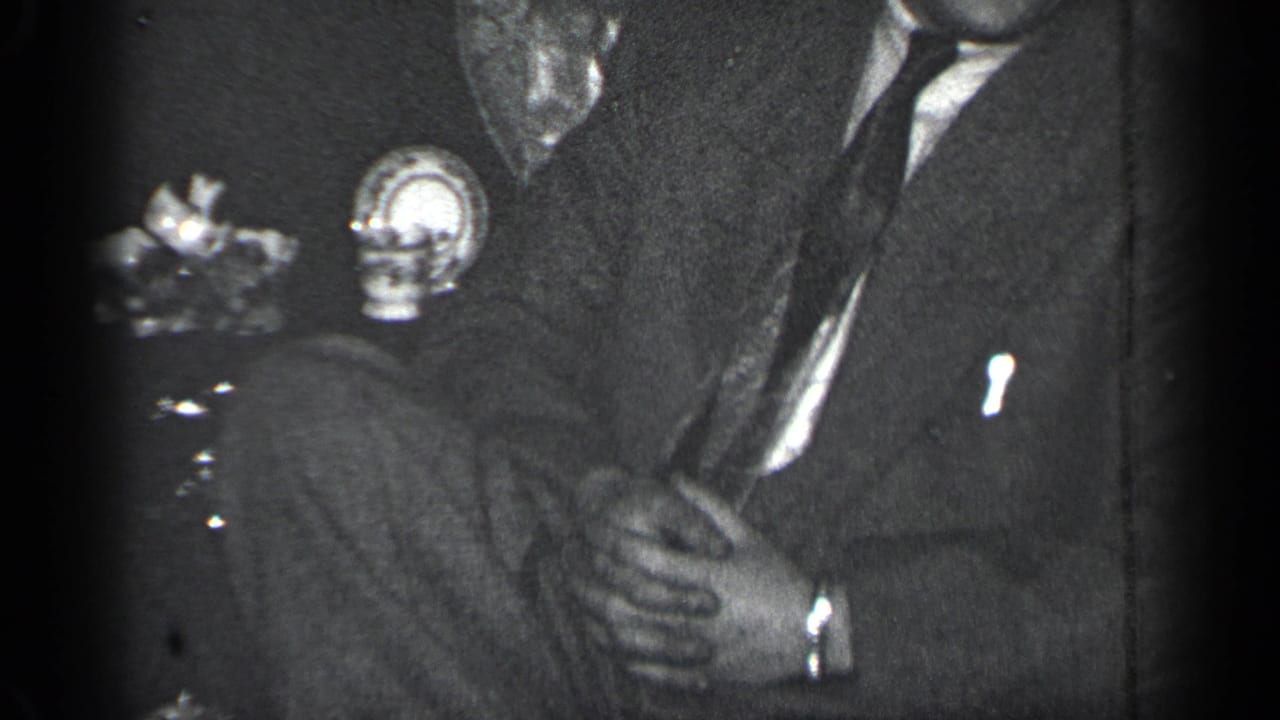 Close view of seated suited men with hands near a small object.