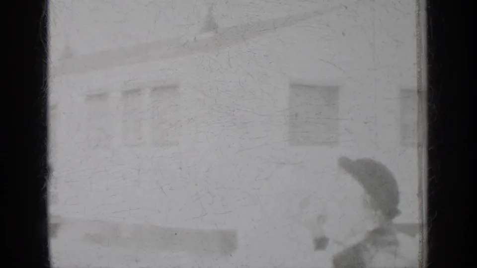 Blurred 1950 New York home-movie frame showing soft building forms and a dark-hatted figure near the lower right edge.