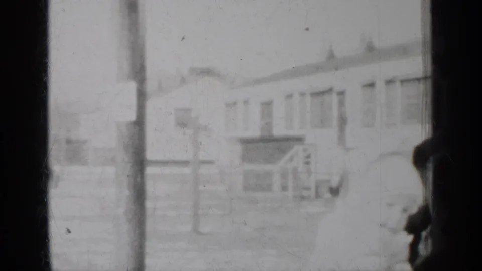 Soft 8mm New York travel frame with a vertical pole, building windows, fencing or railing, and a partial person at the right edge.