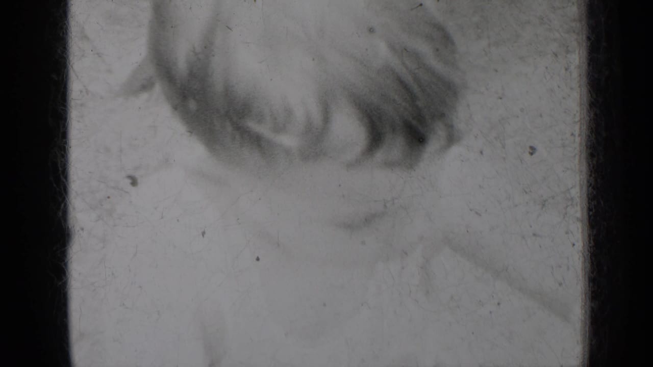 1950 8mm home-movie scan from New York metadata, showing a damaged film area with dark frame edges, dust, scratches, and a loose fiber.