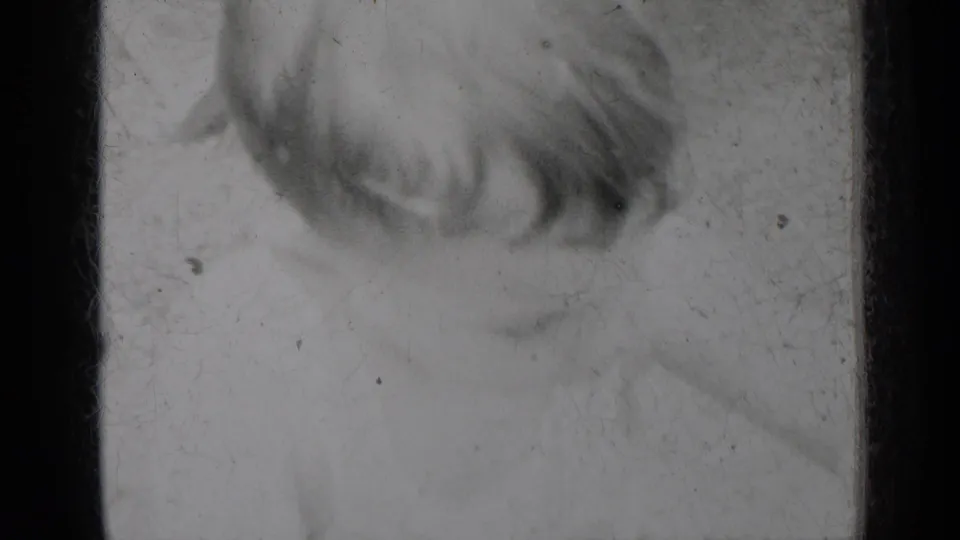 1950 8mm home-movie scan from New York metadata, showing a damaged film area with dark frame edges, dust, scratches, and a loose fiber.