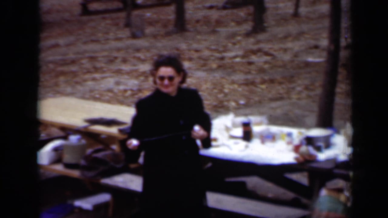 Woman holding a long object beside picnic tables covered with food and supplies.