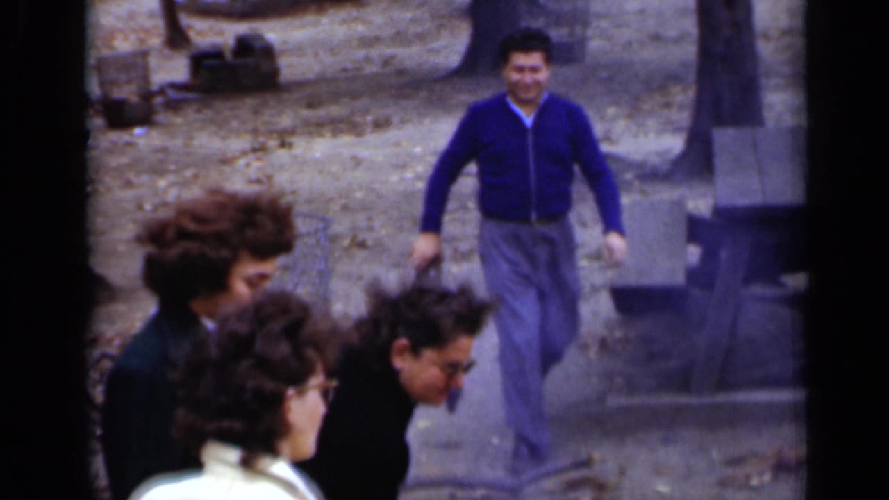 Adults stand in the foreground as a man approaches through the park.