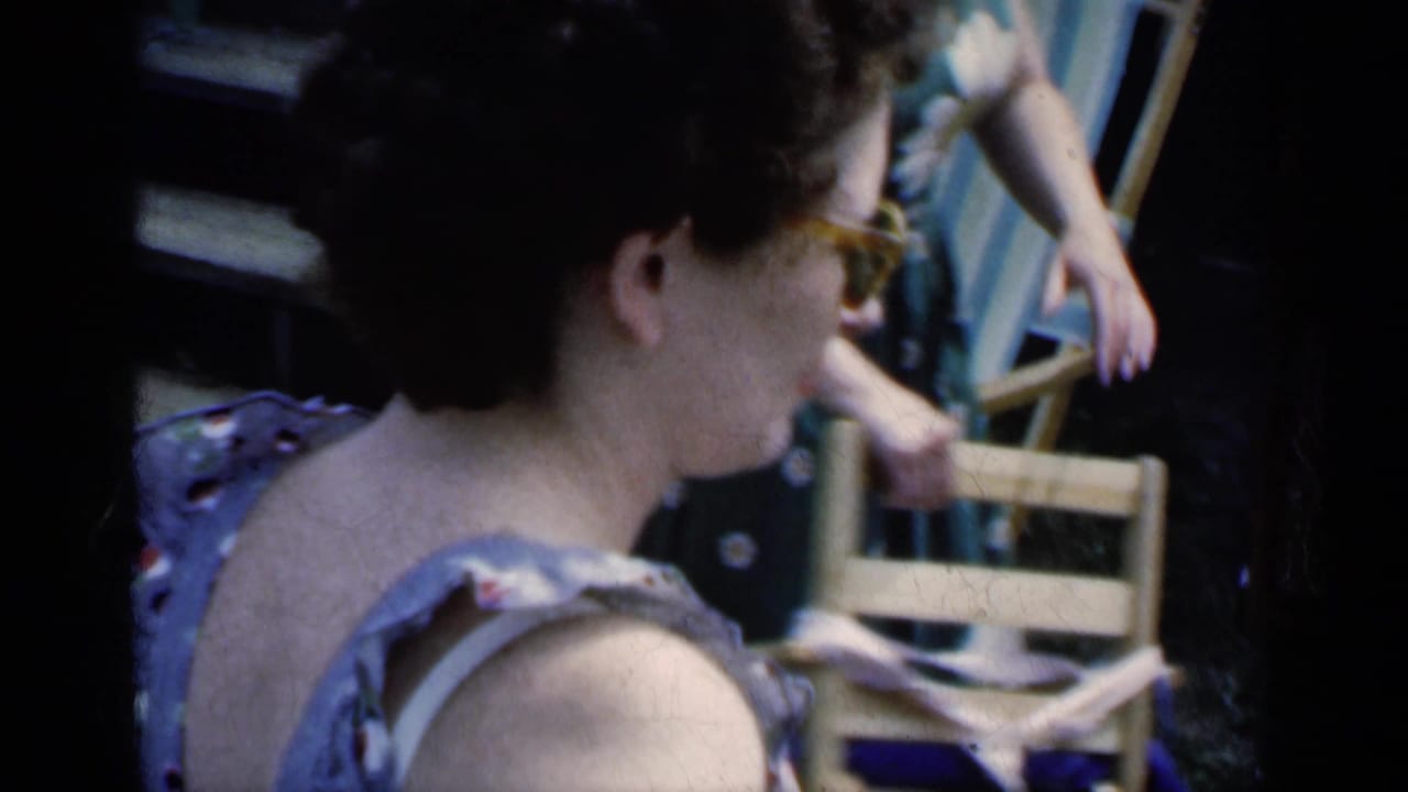 Woman in sunglasses seen from the side near wooden lawn chairs in a sunny backyard.