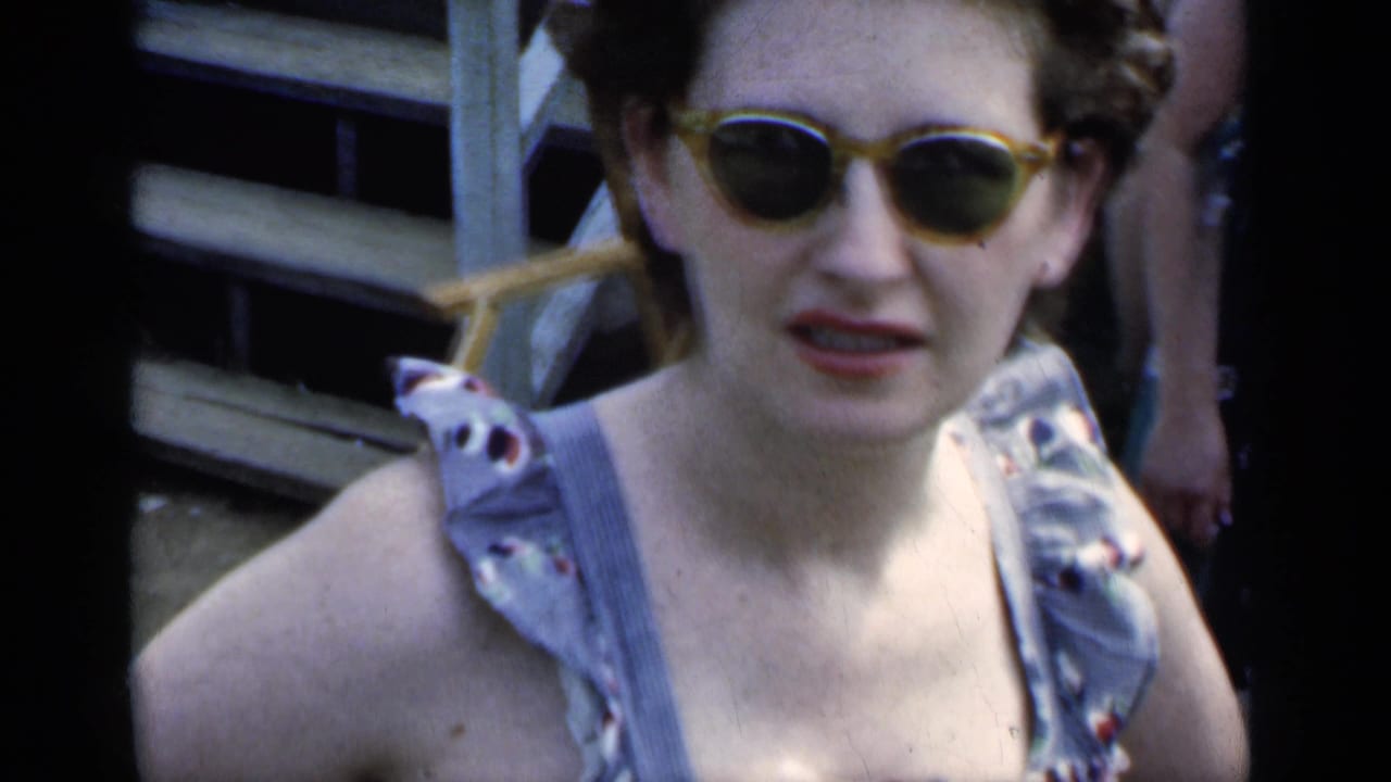 Close view of a woman wearing yellow-framed sunglasses and a sleeveless patterned dress.