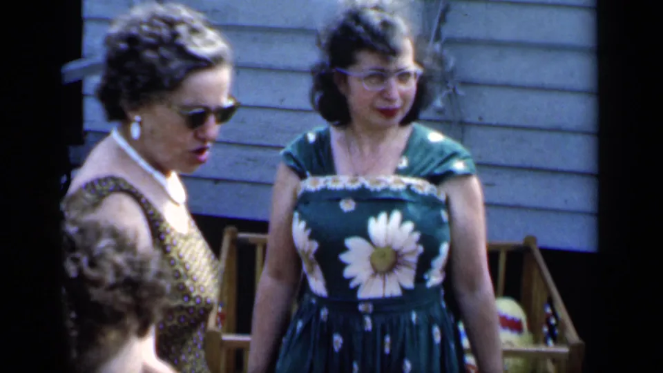 1951 New York home-movie frame of three women in summer dresses, sunglasses, and pearls standing in a backyard.