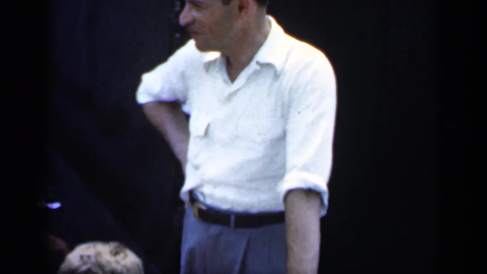 1951 New York home-movie frame of a man in a white short-sleeved shirt standing casually against a dark background.