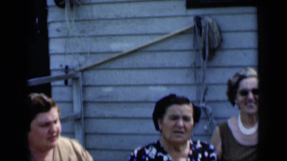 1951 New York home-movie frame with three older women standing together outside a light-sided house.