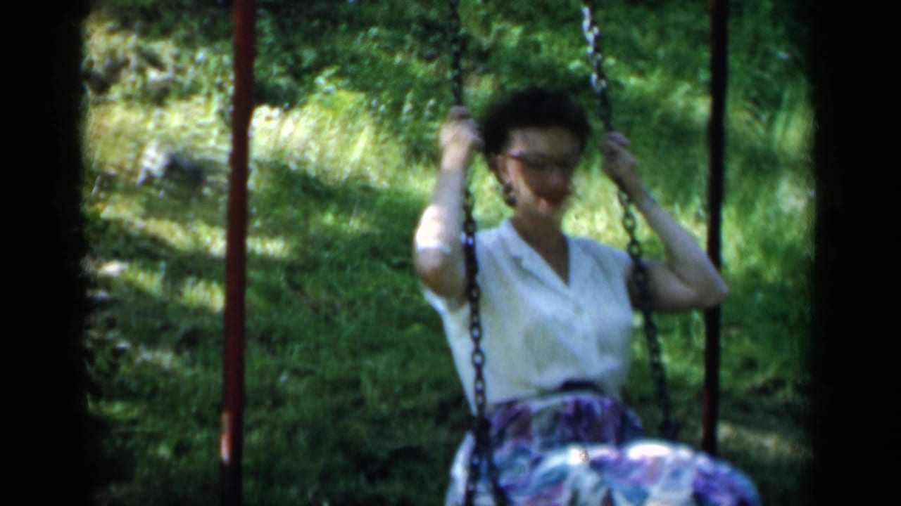 Woman with glasses swings outdoors in front of green foliage.