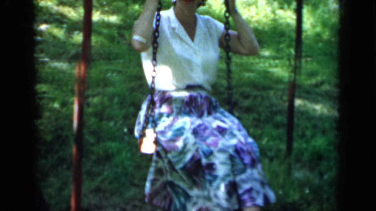 Woman holds the swing chains as her floral skirt moves over a grassy background.