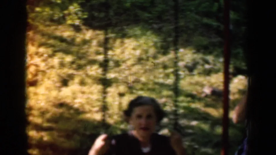 A closer home-movie frame shows the woman's face as she swings toward the camera in a shaded park-like area in New York.