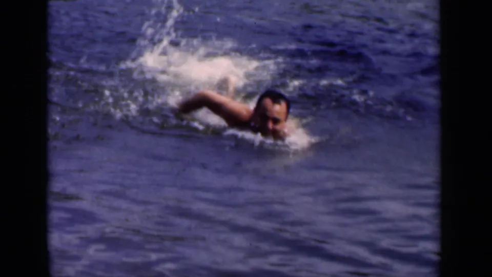 In the lower frame, the adult man swims nearer to camera, his head and arm visible amid ripples and small splashes.