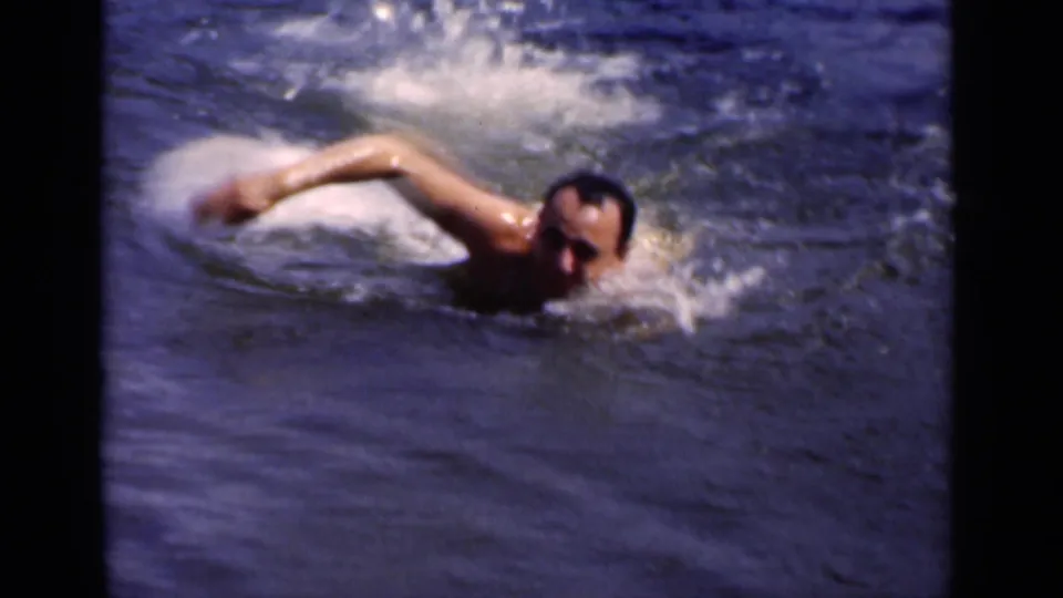 The adult swimmer is seen close in frame, raising one arm in an overhand stroke as water breaks around his shoulder and face.