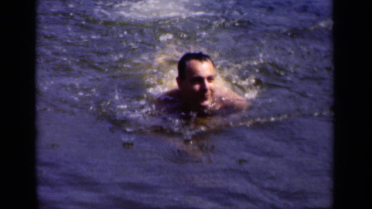 Adult man swimming toward the camera in rippling open water.