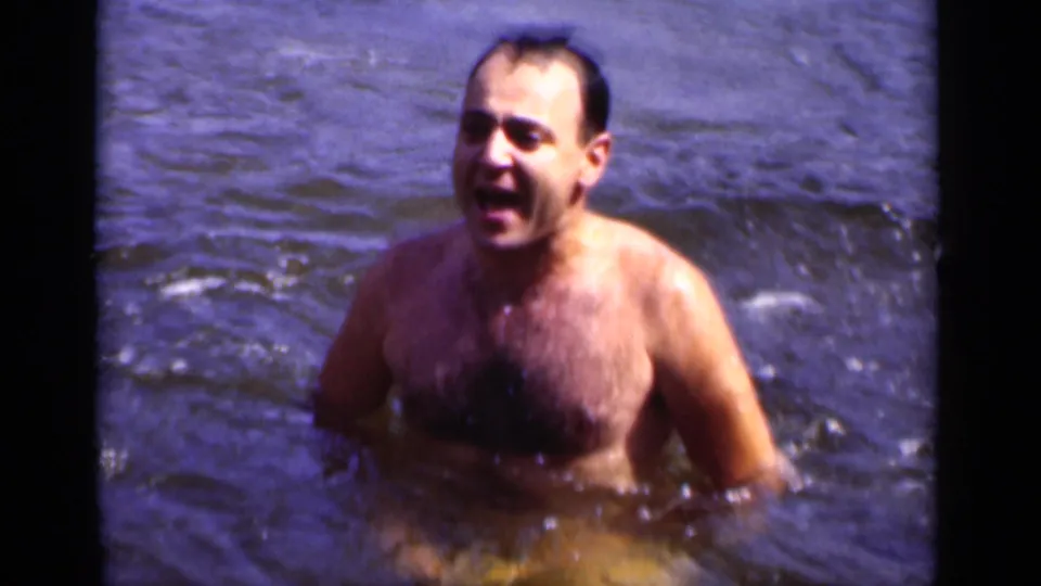 An adult man appears chest-deep in open water, smiling or calling out in the 1951 New York home-movie frame.