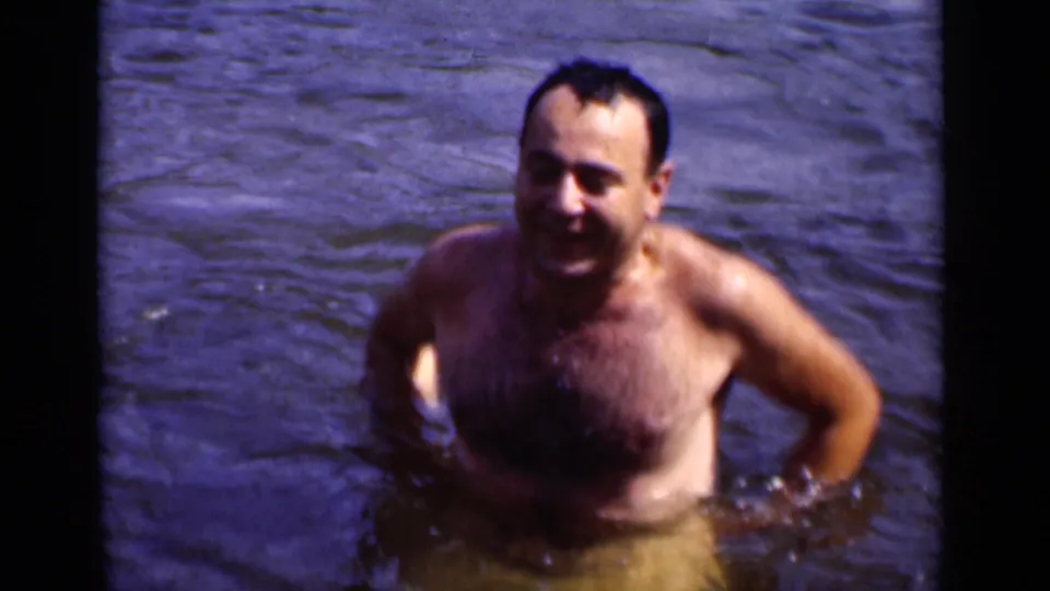 In 1951 New York home-movie footage, a smiling adult man stands chest-deep in open water with dark film borders visible.