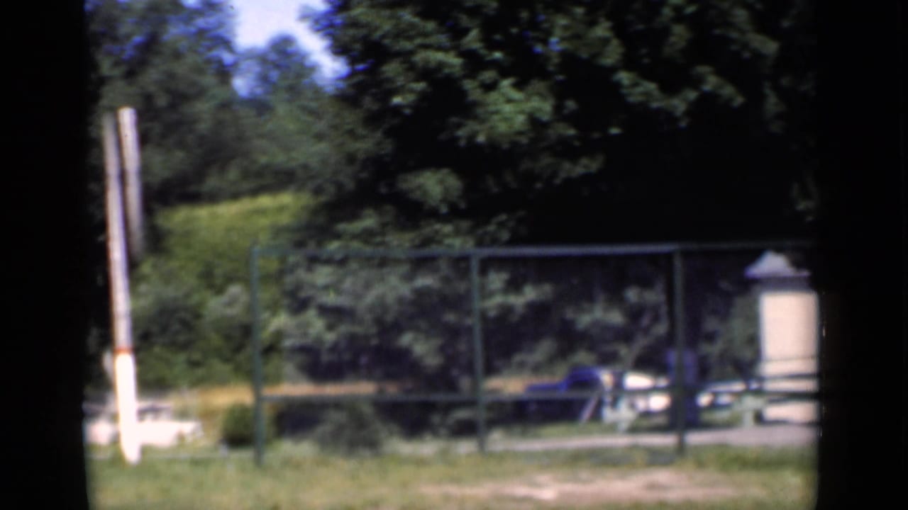 Fence, trees, parked blue car, and light-colored roadside structure near the hotel grounds.
