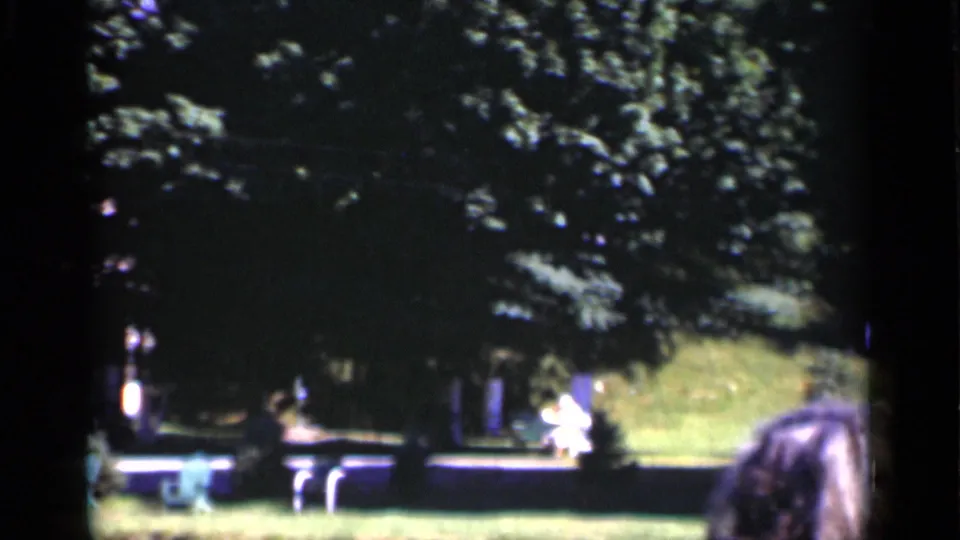 1951 New York 8mm frame showing a shaded lawn, trees, chairs, and distant people relaxing outdoors.