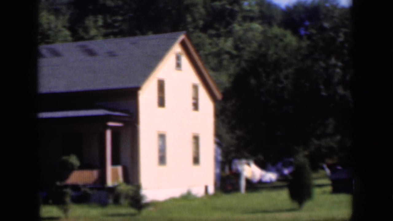 1951 New York home-movie view of a pale two-story house on a green plot with trees and laundry nearby.