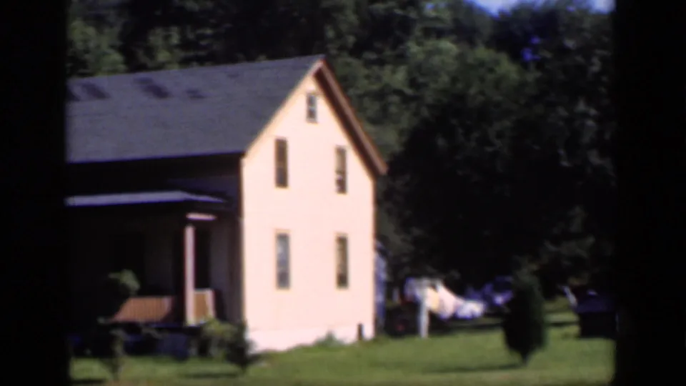 1951 New York home-movie view of a pale two-story house on a green plot with trees and laundry nearby.