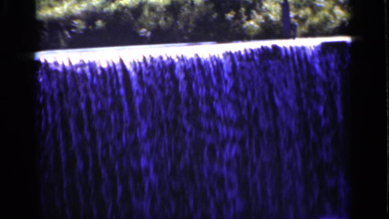 Wide blue-toned waterfall dropping over a bright ledge with trees above.