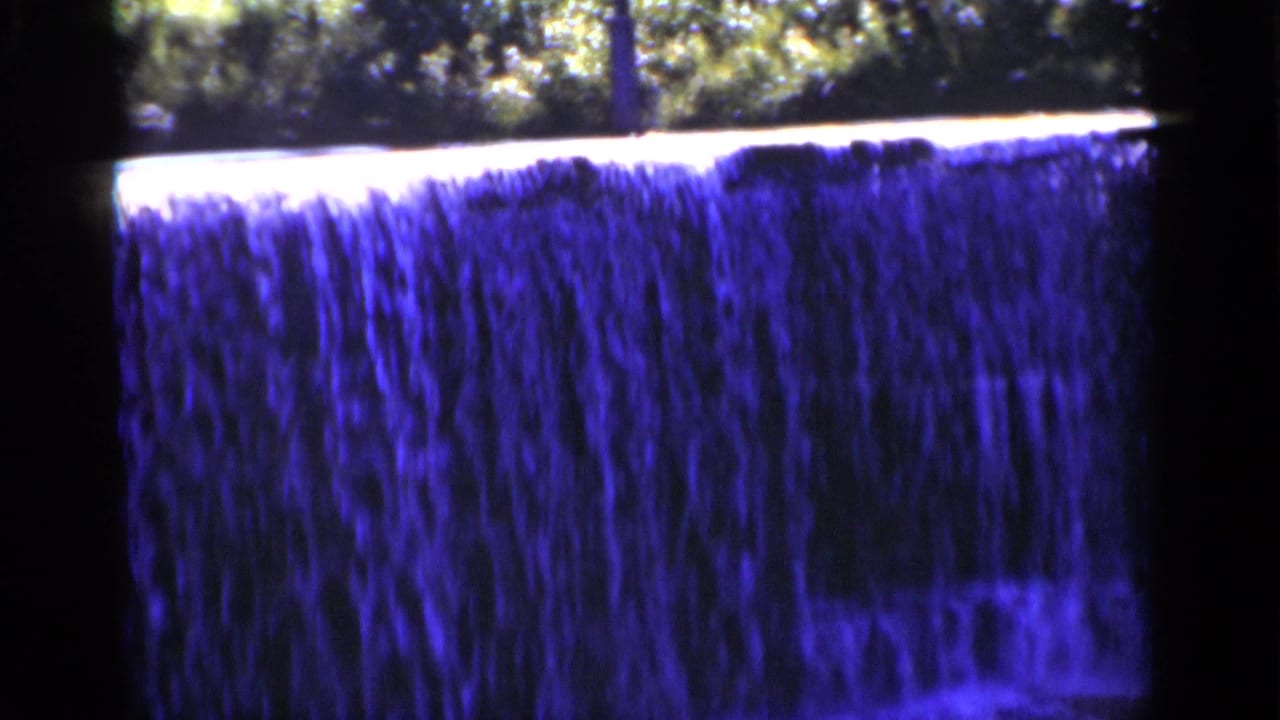 Close view of a wide waterfall with trees above and dark film borders.