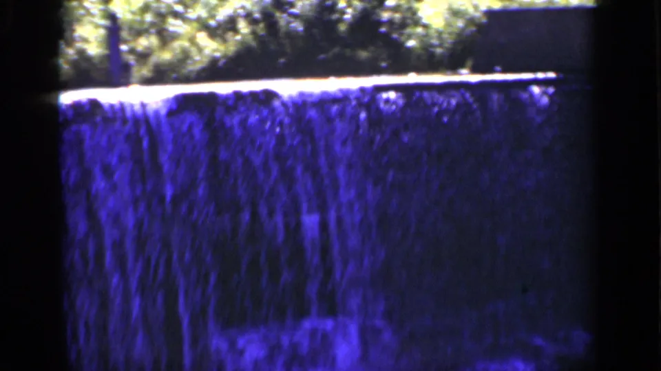 1951 New York 8mm frame showing water flowing over a ledge into a shadowed pool area, with trees above and blue color shift.