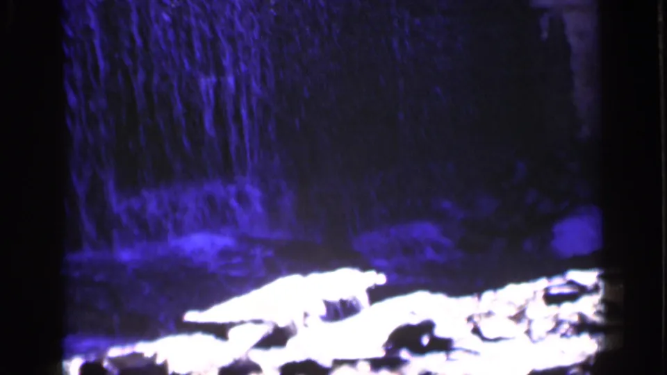 1951 New York 8mm frame focused on the base of the waterfall, where blue water splashes near bright rocks in shadow.