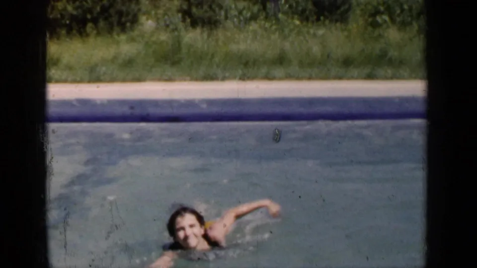 In 1951 New York home-movie footage, a child swims in blue-green pool water with grass visible beyond the pool edge.