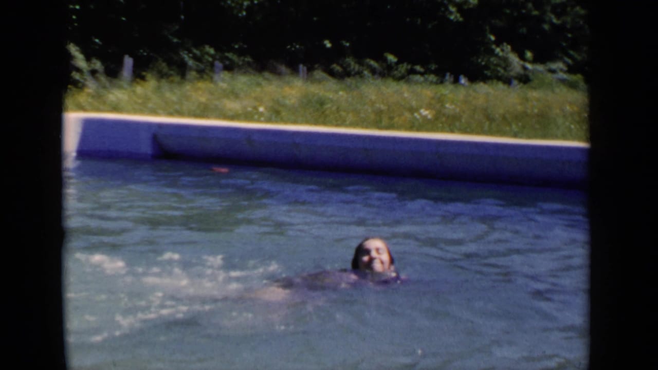 1951 New York 8mm frame showing a swimmer partly above the water in an outdoor pool bordered by grass and trees.